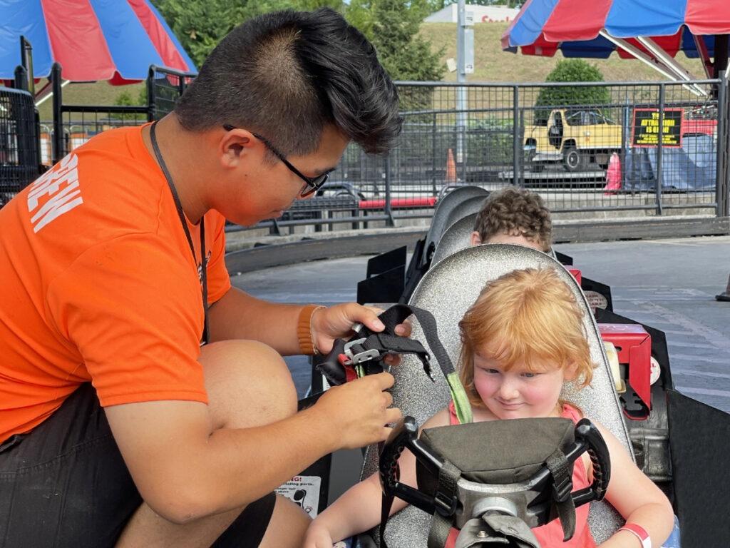 A NASCAR SpeedPark employee helping a kid get strapped in a go kart