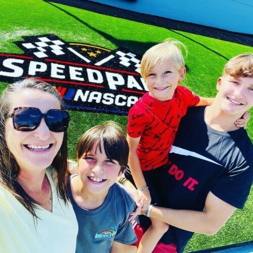 a mother and her kids taking a selfie in front of the logo of NASCAR Speedpark