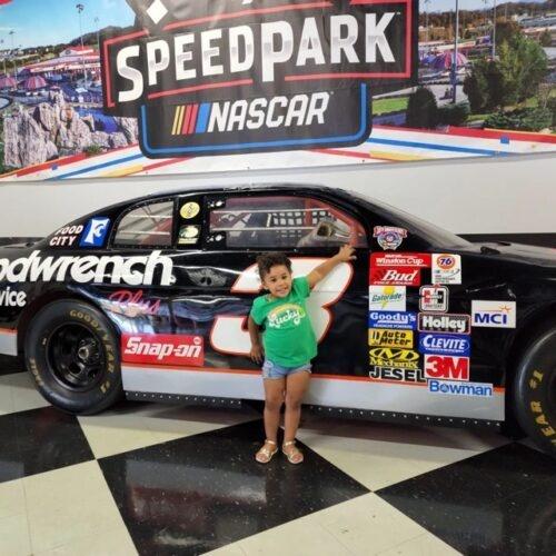 a little girl posing in front of a NASCAR car